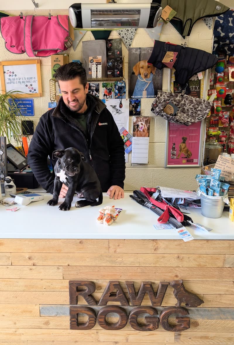 The owner behind the carved wooden counter with a small dog